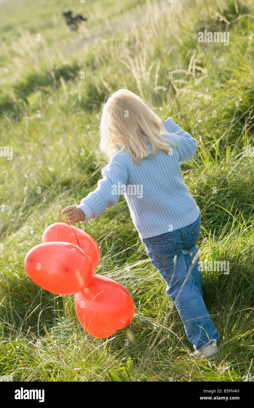 Little girl (3-4) walking with balloons in the meadow, rear view Stock ...