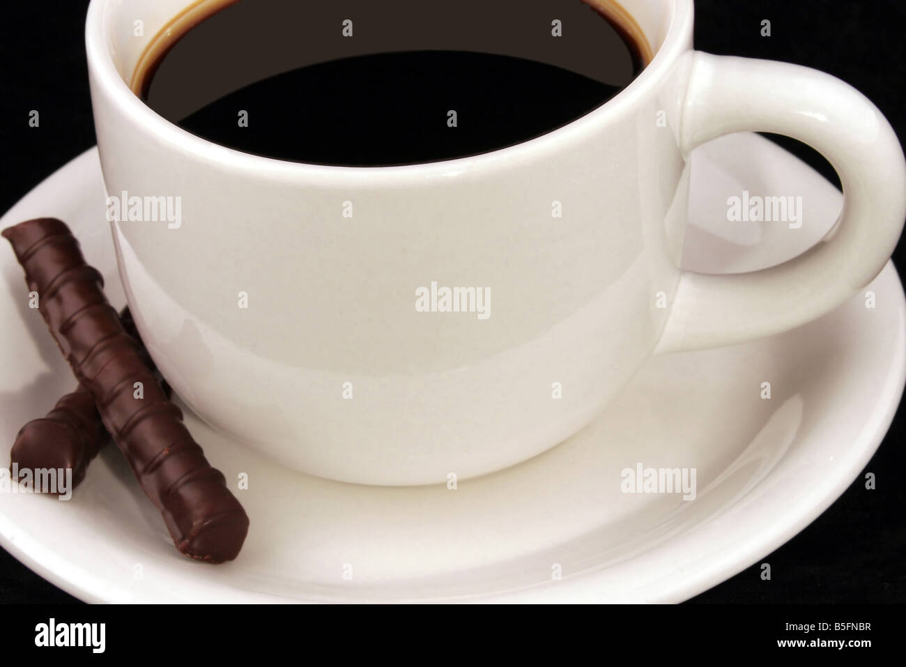 A white cup filled with black coffee and two chocolates resting on the saucer. Stock Photo