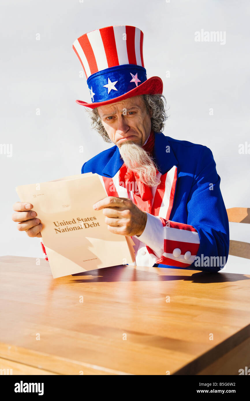 Portrait of Uncle Sam sitting at a table with tears in his eyes while reading the National Debt Stock Photo
