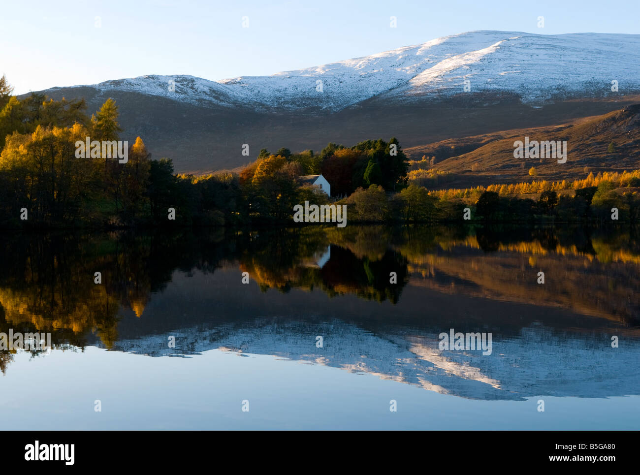Loch Alvie showing Autumn colours and calm reflection of snowy mountains Stock Photo