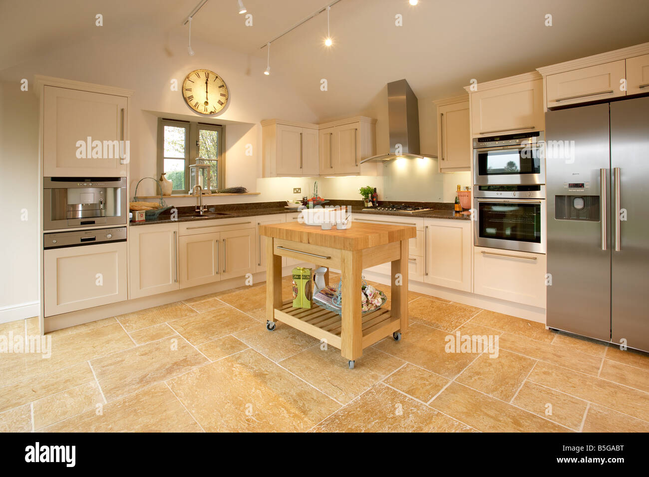 Modern shaker style kitchen with limestone floor, butchers block and stainless steel appliances Stock Photo