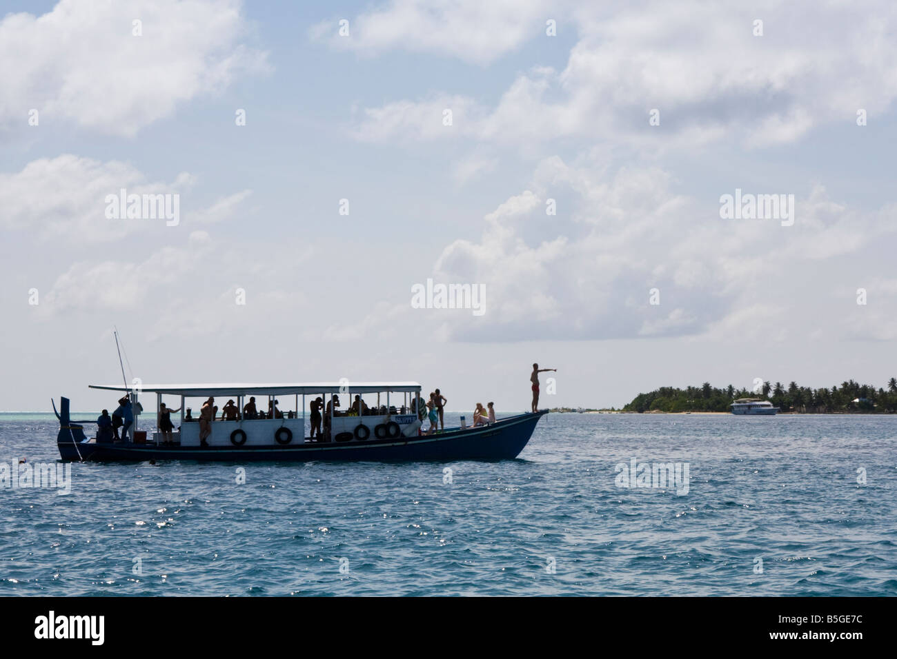 A boat full of tourists moving past an island in The Maldives Stock Photo