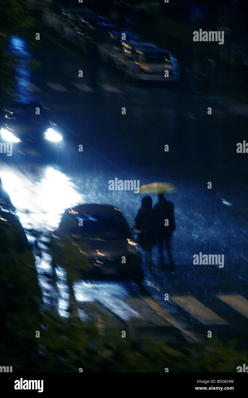 two people walking in heavy rain at night in town Stock Photo