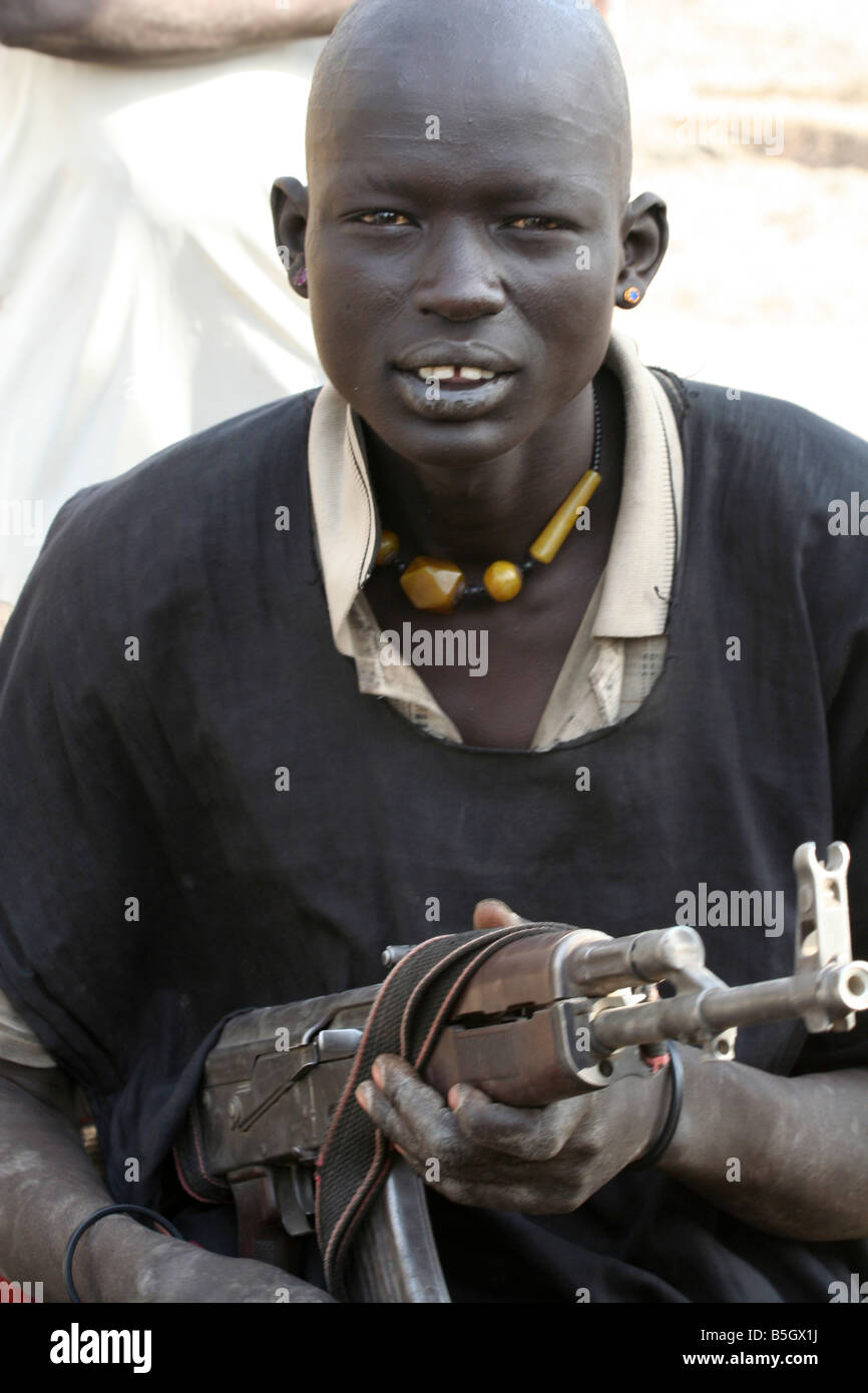 A young Dinka man in a cattle camp near Rumbek, South Sudan keeps his AK-47 close. Stock Photo