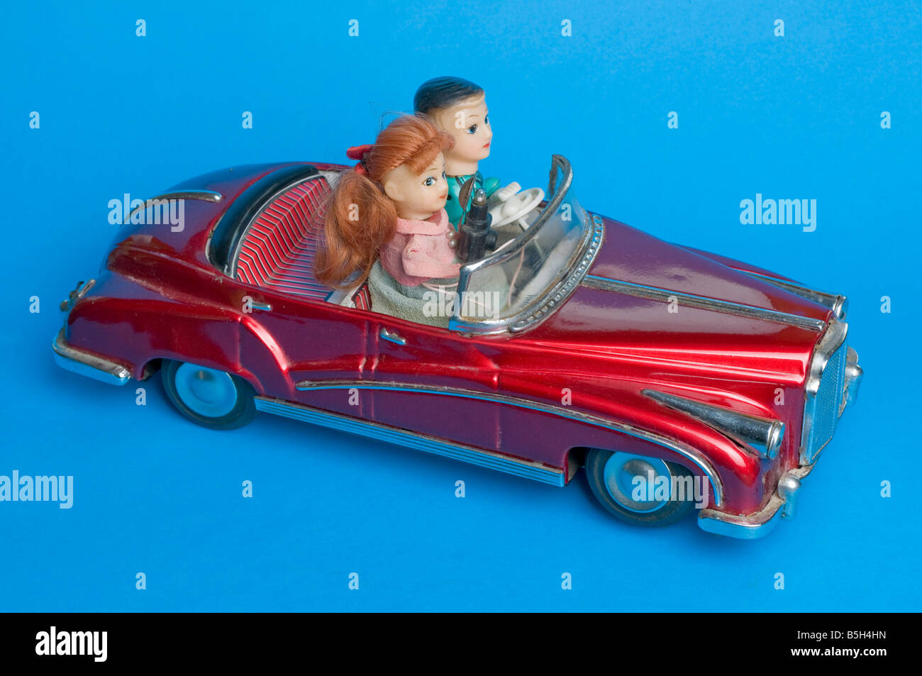 Pressed metal novelty toy battery powered car with driver sitting beside a woman photographer with camera and flash. Stock Photo