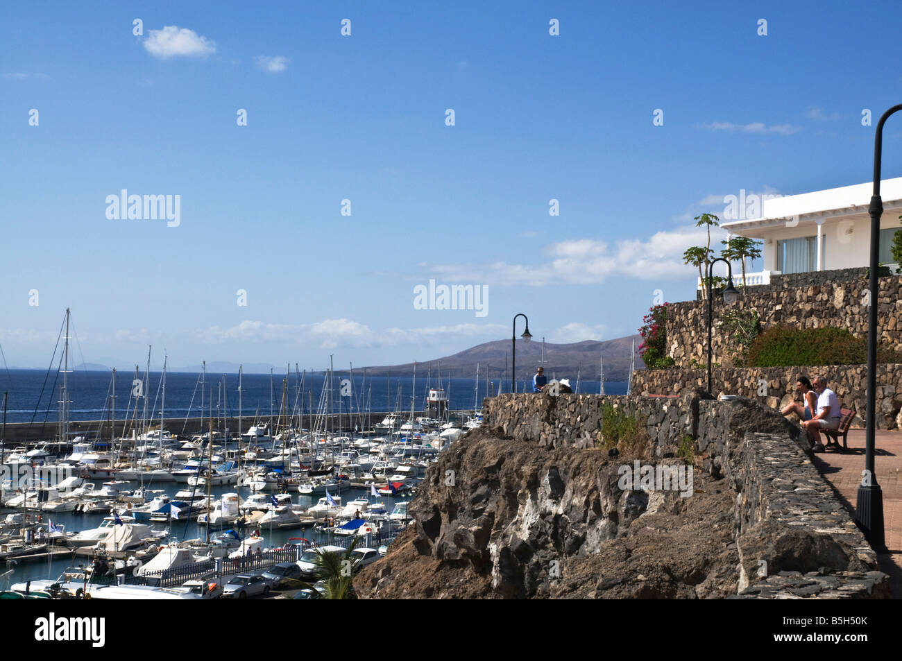 dh  PUERTO CALERO LANZAROTE Tourist Holidaymaker people couple sitting on bench overlooking marina Stock Photo