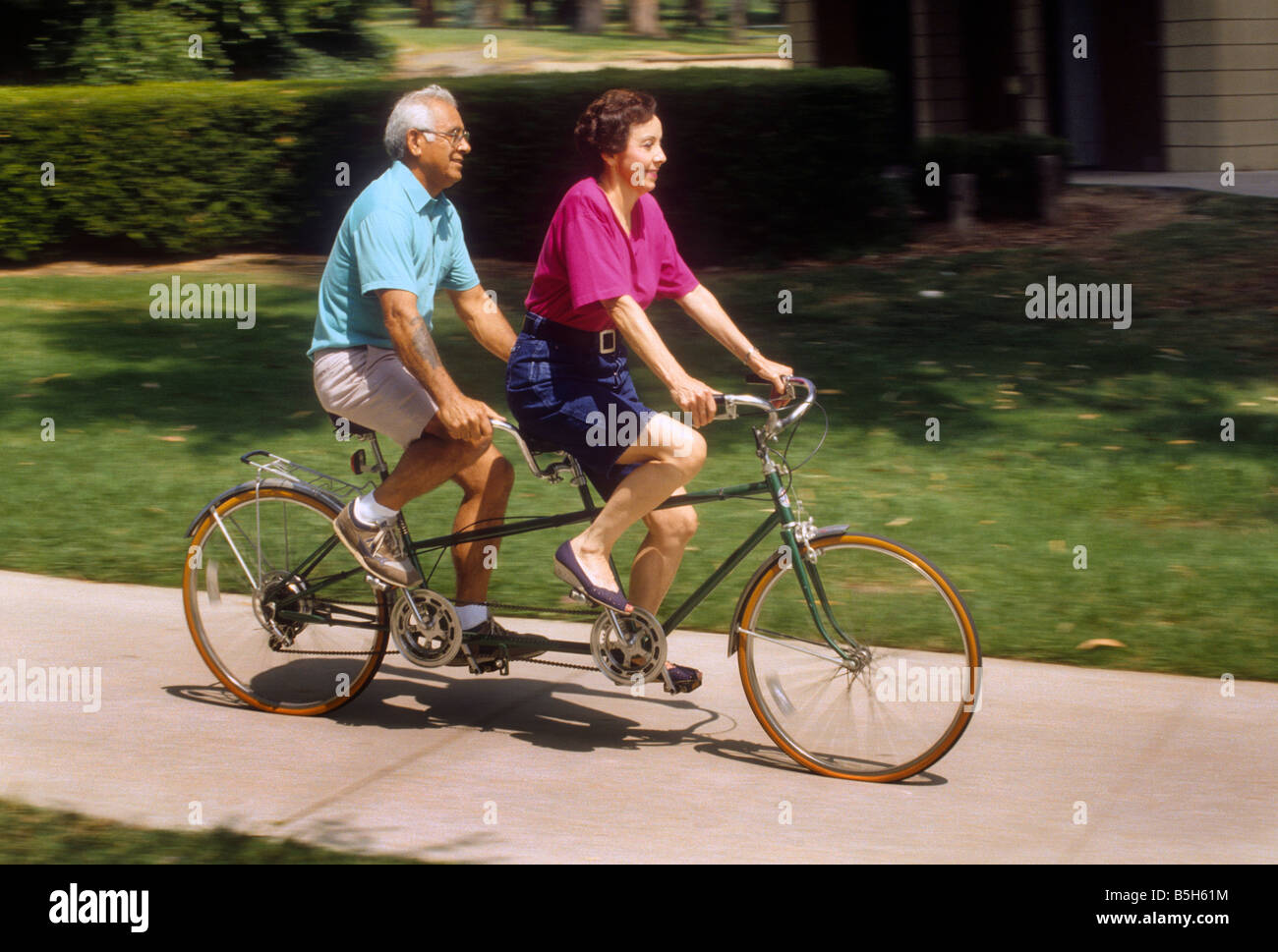 Senior Hispanic couple rides tandem bicycle on sidewalk Stock Photo Alamy
