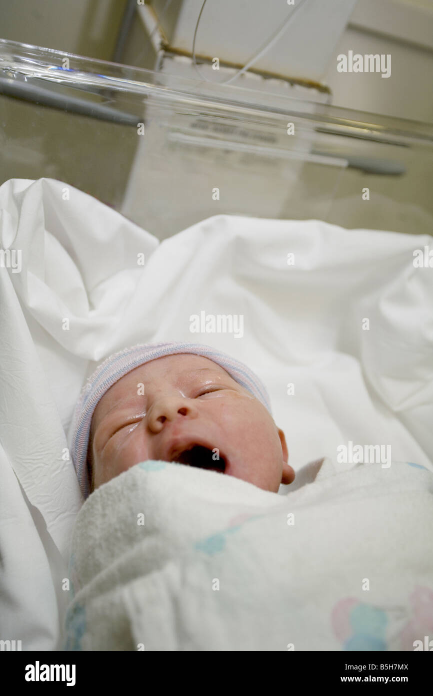 A newborn infant wrapped in a blanket yawning in a bed in the hospital ...