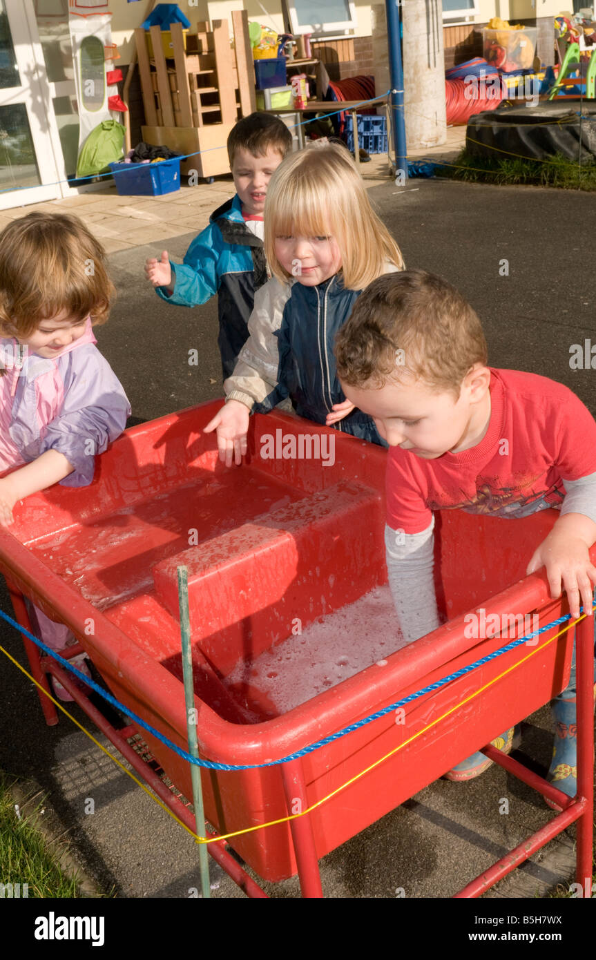 four kids young children in nursery kindergarten day care centre playing with water outdoors Stock Photo