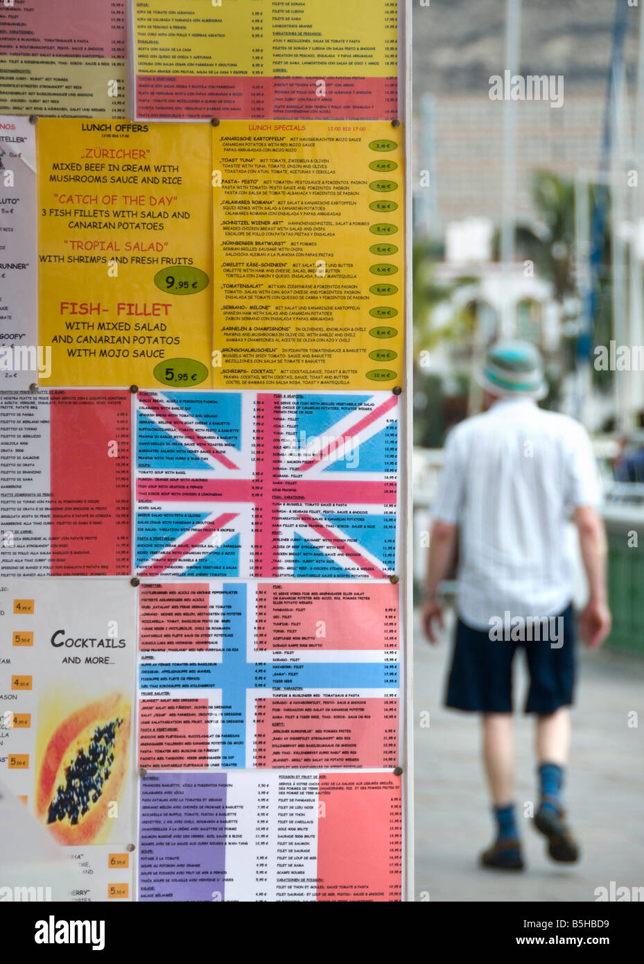 Multilingual menu board with national flags to attract foreign tourists with stereotypical British tourist behind Stock Photo