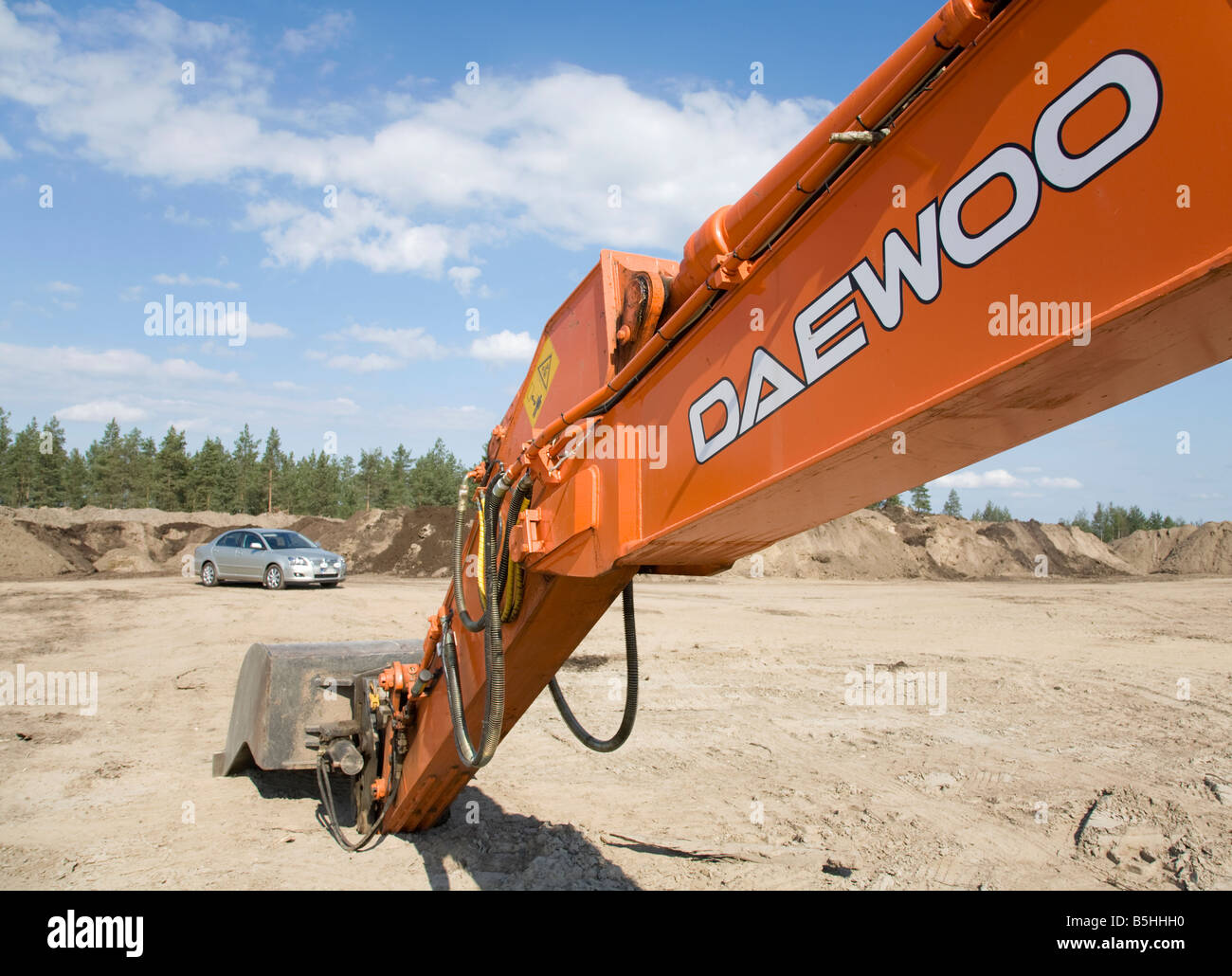 Orange Daewoo digger boom extended and Toyota Avensis car , Finland Stock Photo