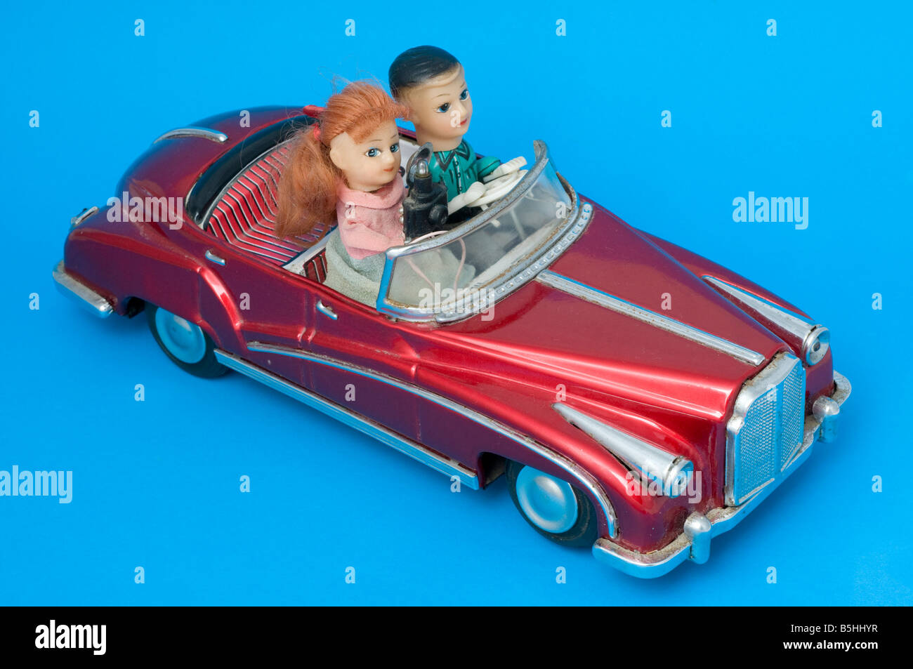 Pressed metal novelty toy battery powered car with driver sitting beside a woman photographer with camera and flash. Stock Photo