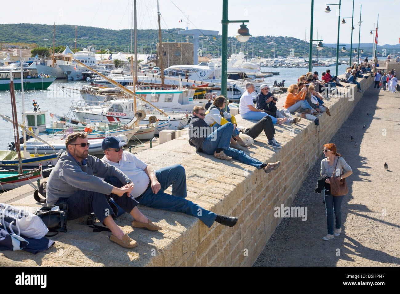 Tourists sit on a wall in the port of Saint-Tropez / Cote d'Azur / Provence / Southern France Stock Photo