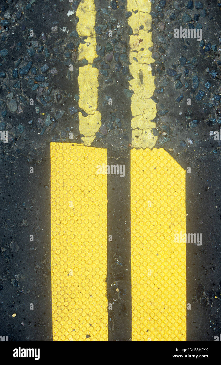 Double yellow lines on black tarmac road where part has been repaired with stick-on lines which fail dismally to match original Stock Photo