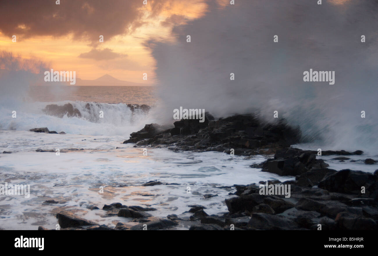 Waves crashing onto rocks at sunset. El Confital, Las Palmas, Gran Canaria. Galdar in the distance Stock Photo