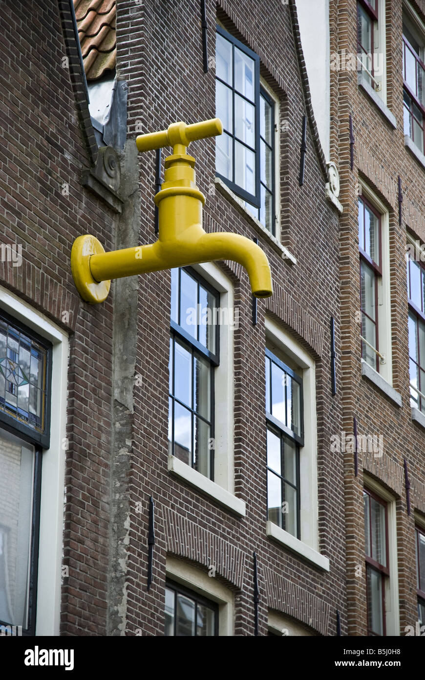 A large yellow faucet art installation protrudes from a building in Amsterdam. Stock Photo