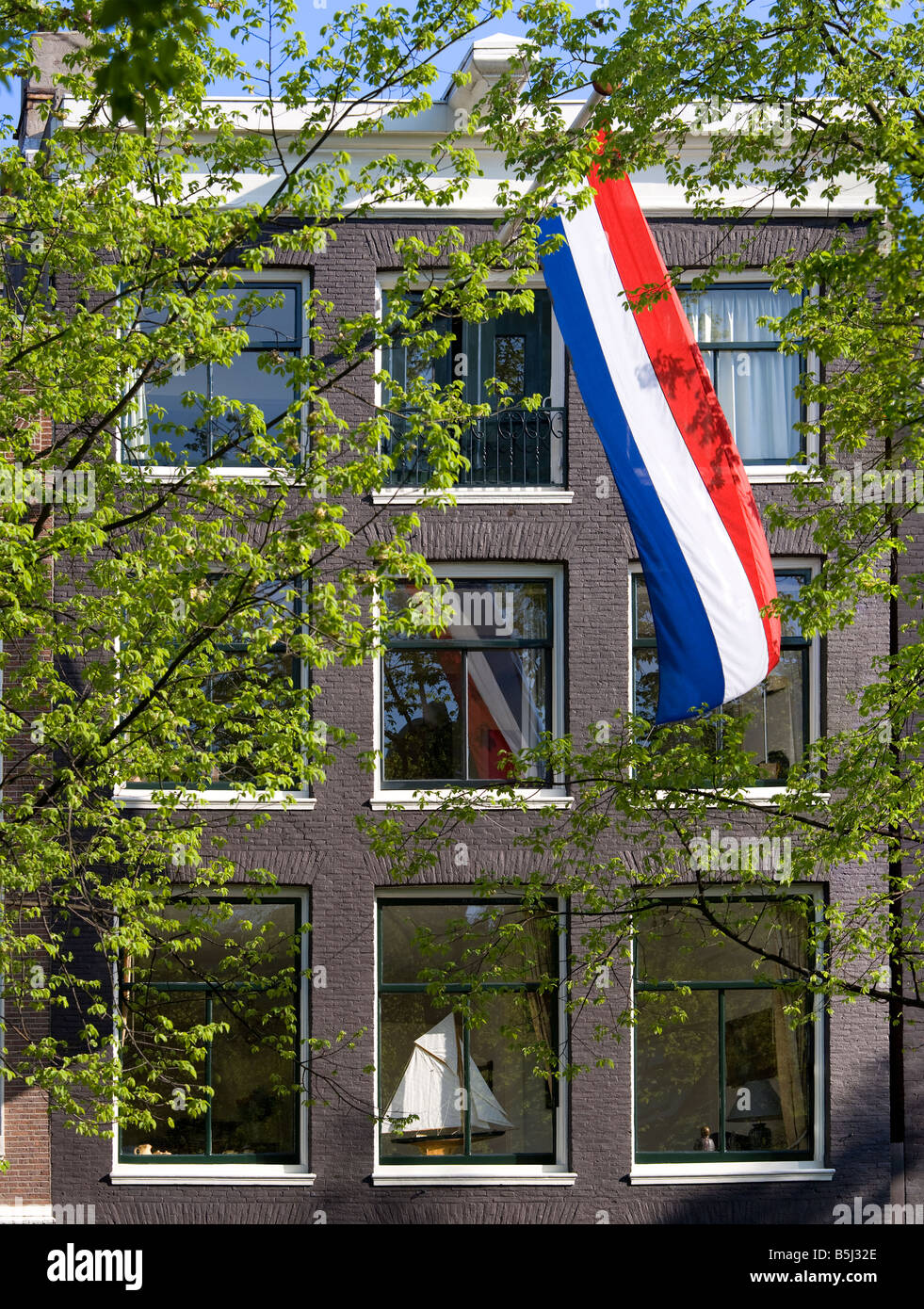 Amsterdam. House on a canal in the Jordaan with Dutch national flag and a model sailing-boat on the windowsill. Springtime. Stock Photo