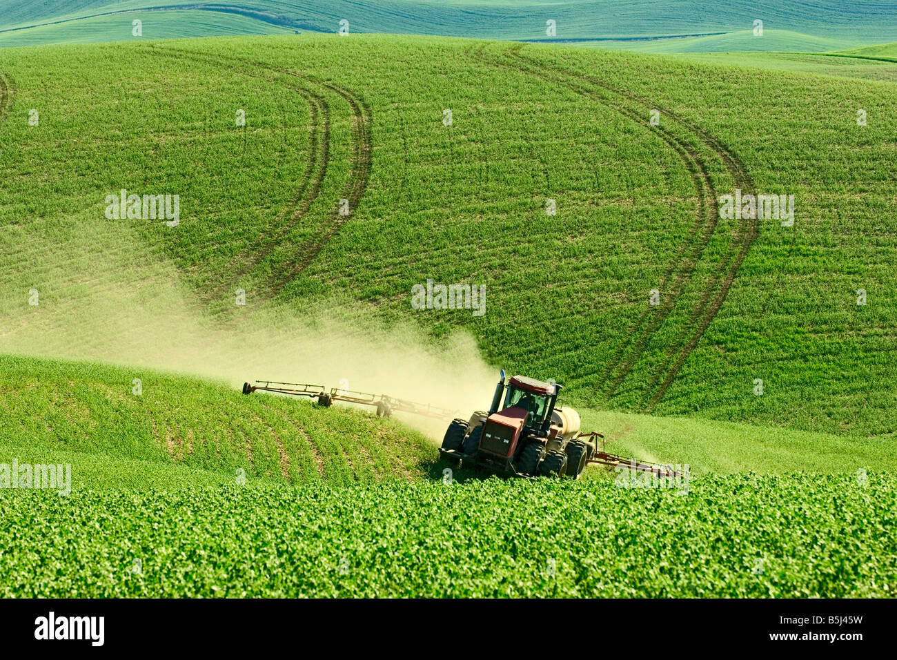 A tractor pulling a sprayer sprays garbanzo beans in the spring in the Palouse region of Washington Stock Photo