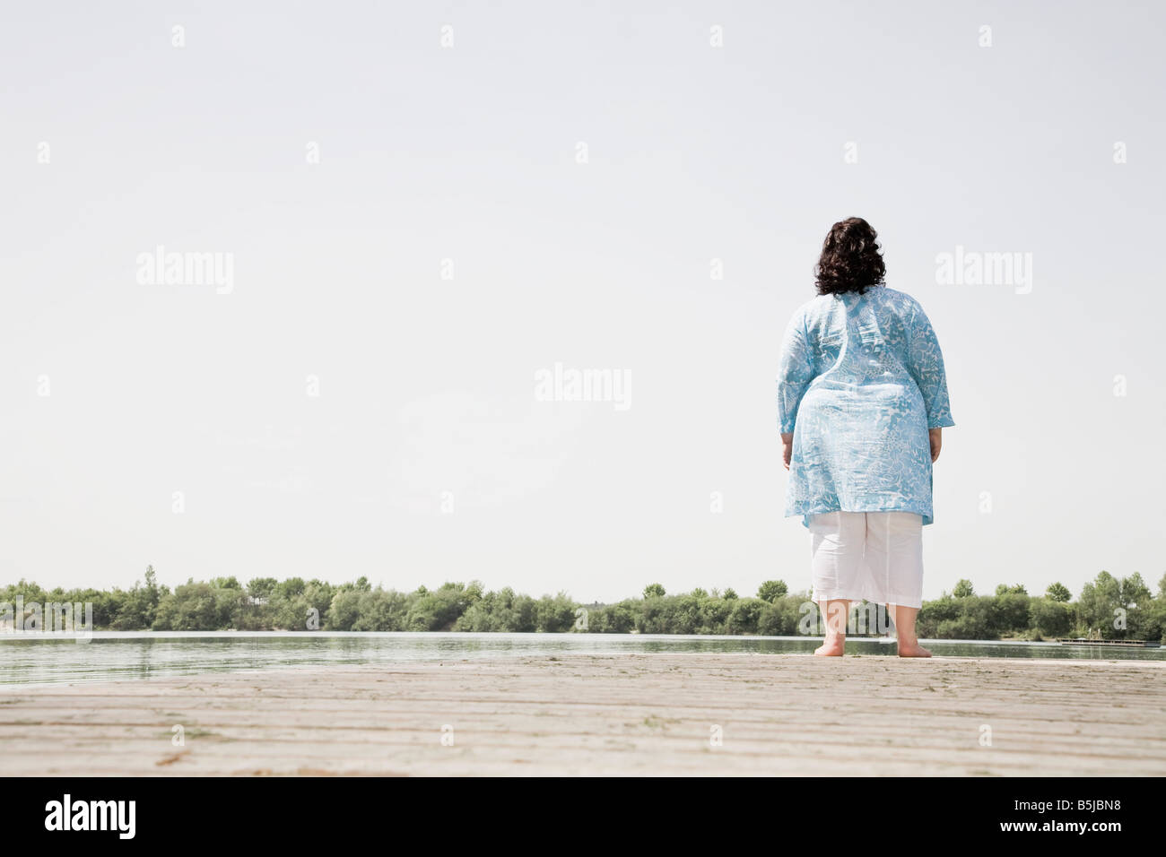 rear view view of overweight woman standing on pier by lake Stock Photo