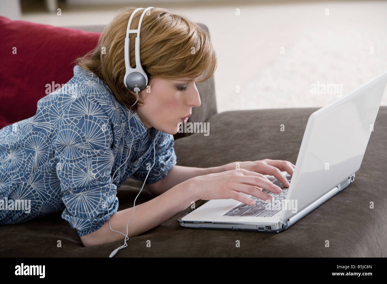 young woman at home wearing headset while working with laptop computer ...