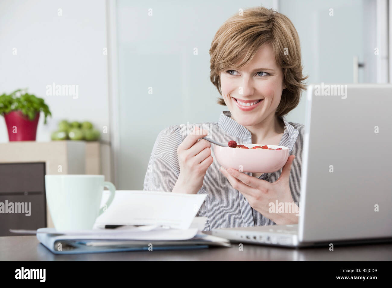 portrait of woman at home in front of computer eating snack Stock Photo