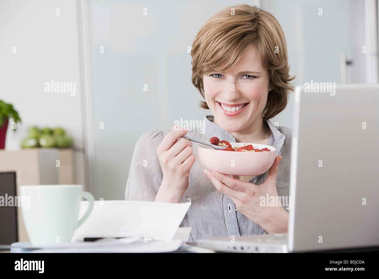 portrait of woman at home in front of computer eating snack Stock Photo