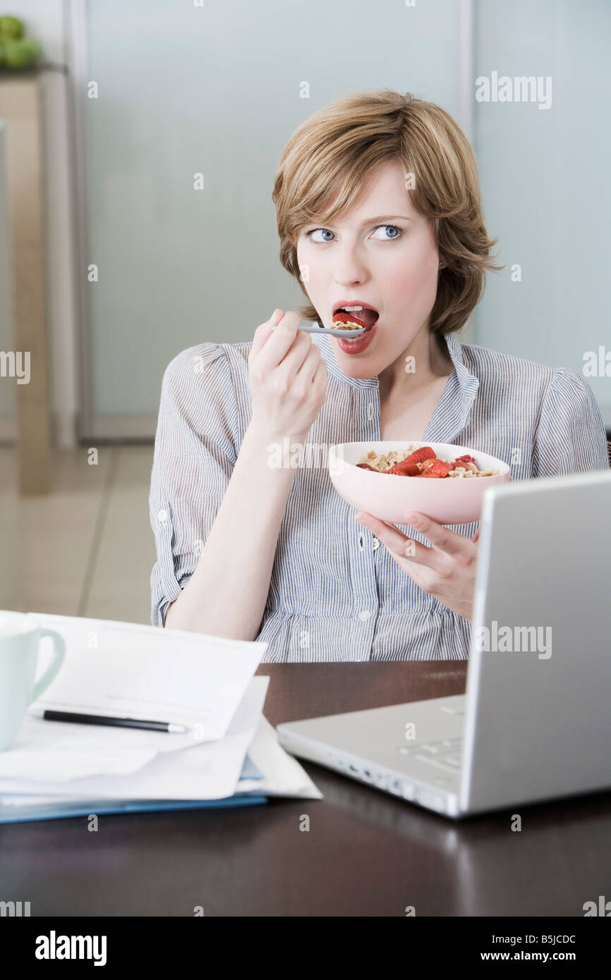 portrait of woman at home in front of computer eating snack Stock Photo