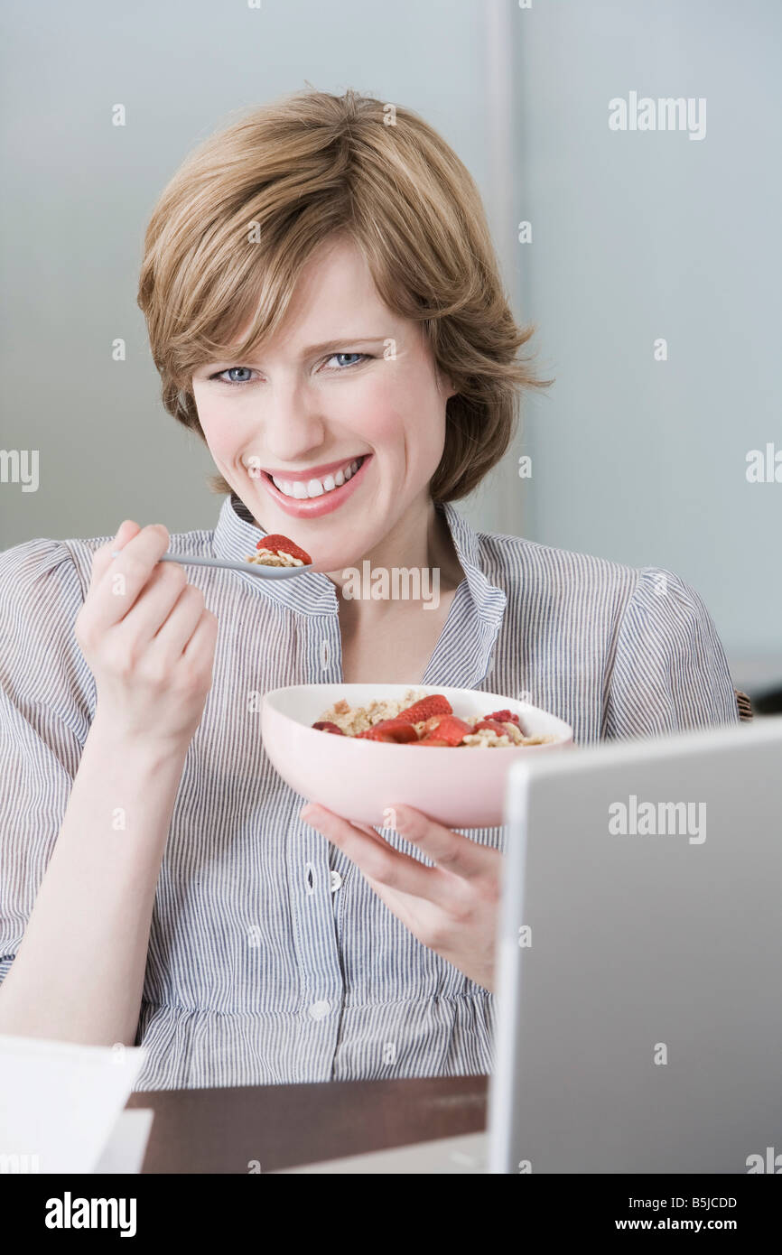 portrait of woman at home in front of computer eating snack Stock Photo
