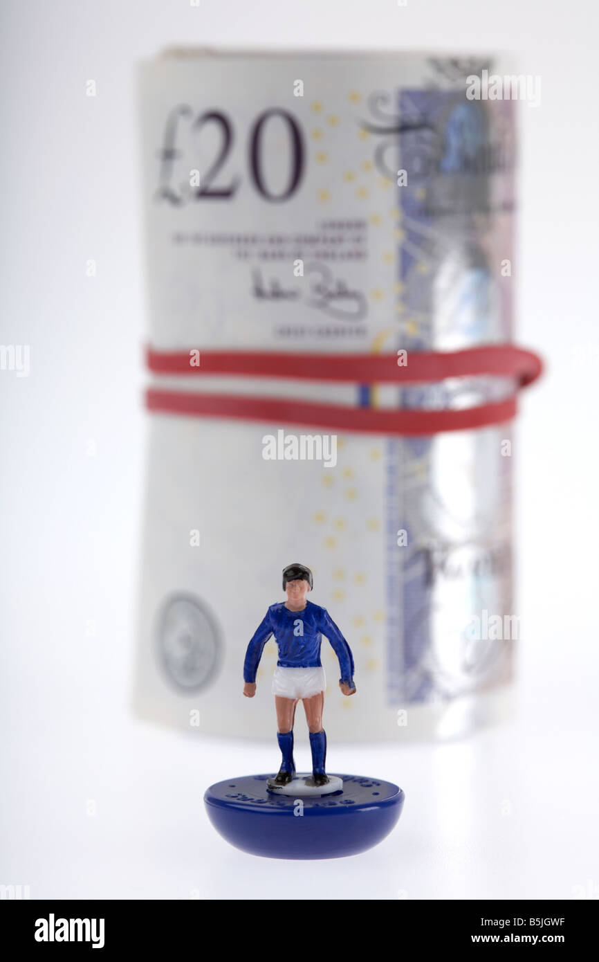 wad of 20 pounds sterling bank notes cash tied up in a roll with elastic band behind toy footballer Stock Photo