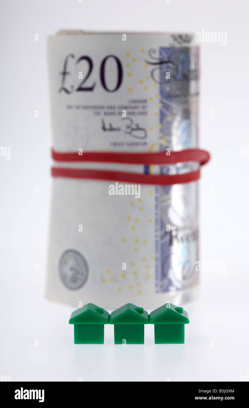 three green houses on front of a wad of 20 pounds sterling bank notes cash tied up in a roll with elastic band Stock Photo