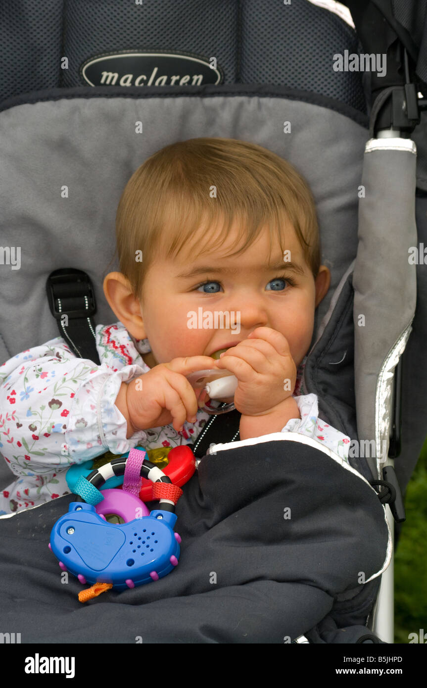 Baby Girl Child sitting sat in a Pushchair Chewing On a Teething Ring Stock Photo
