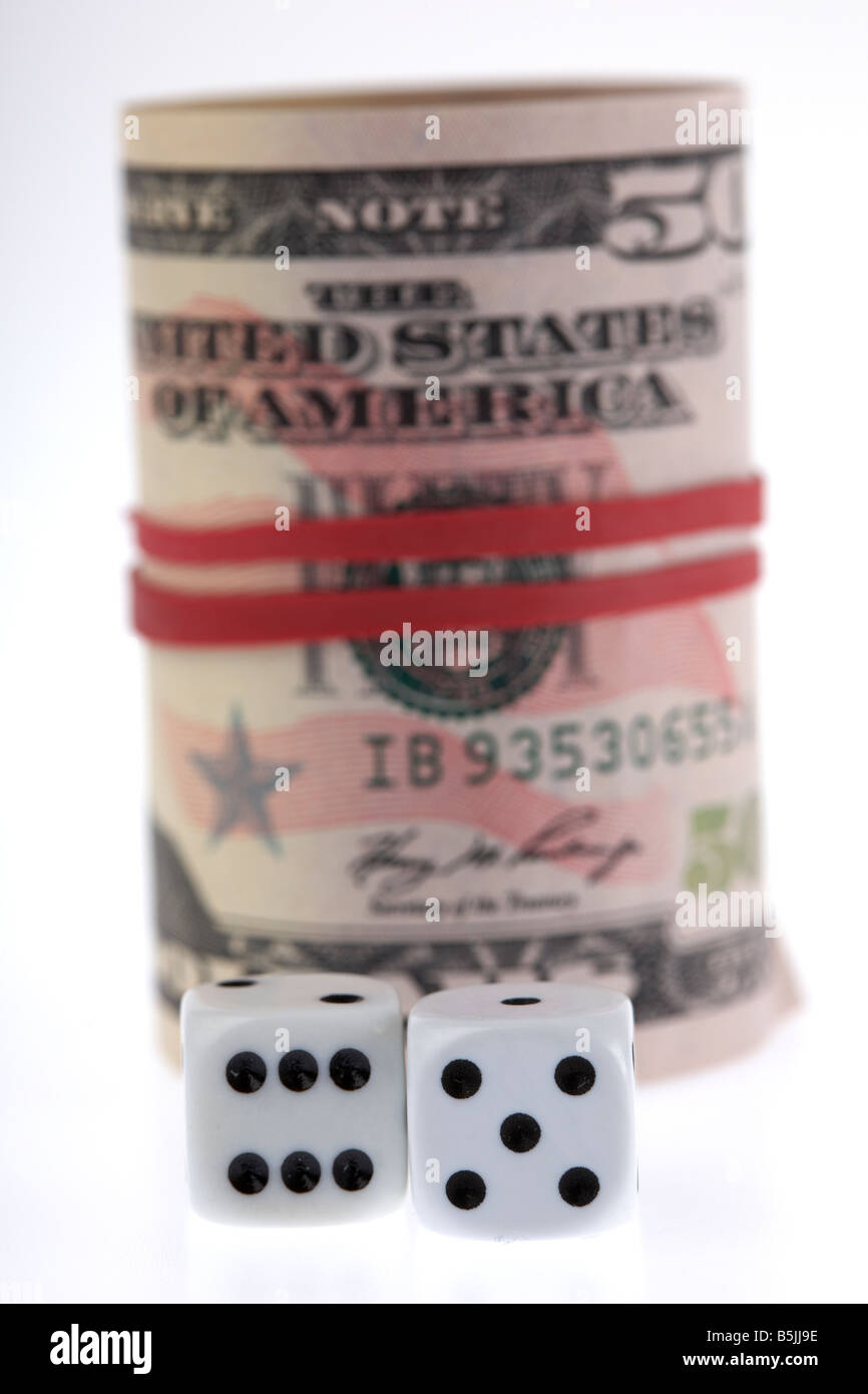 two dice in front of a wad of 50 usa dollar bank notes cash tied up in a roll with elastic band Stock Photo