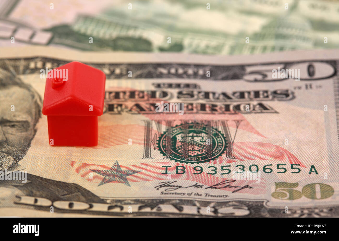 one red house on top of a pile of 50 usa dollar bank notes cash concept for home loans property real estate housing us economy mortgages debt crisis Stock Photo