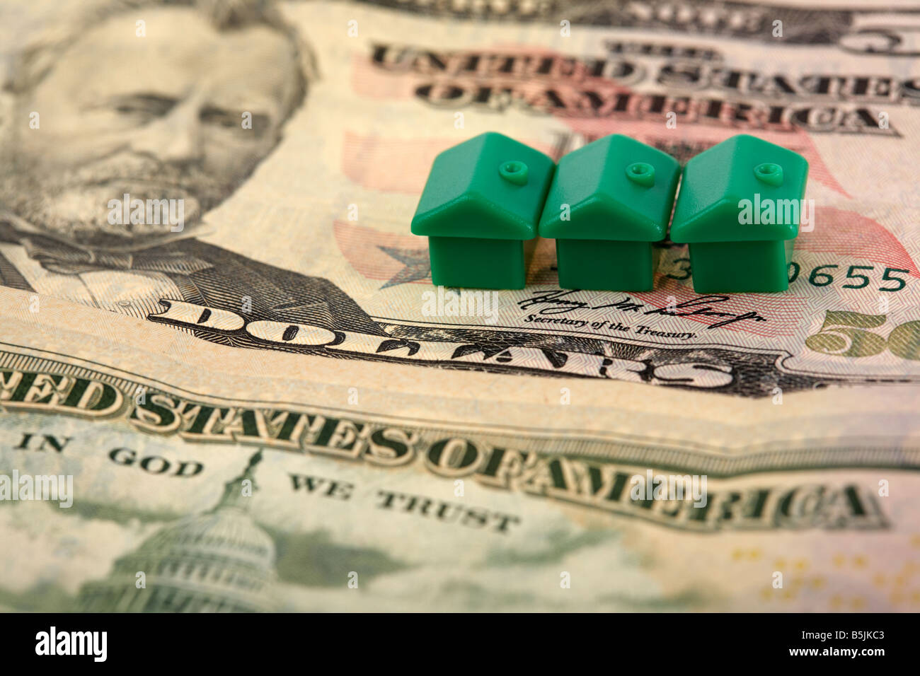 three green houses on top of a pile of 50 usa dollar bank notes cash Stock Photo