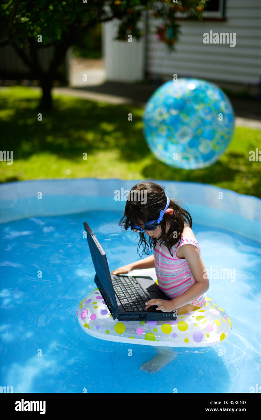 Five year old girl in paddling pool with inflatable rubber ring and laptop computer Stock Photo