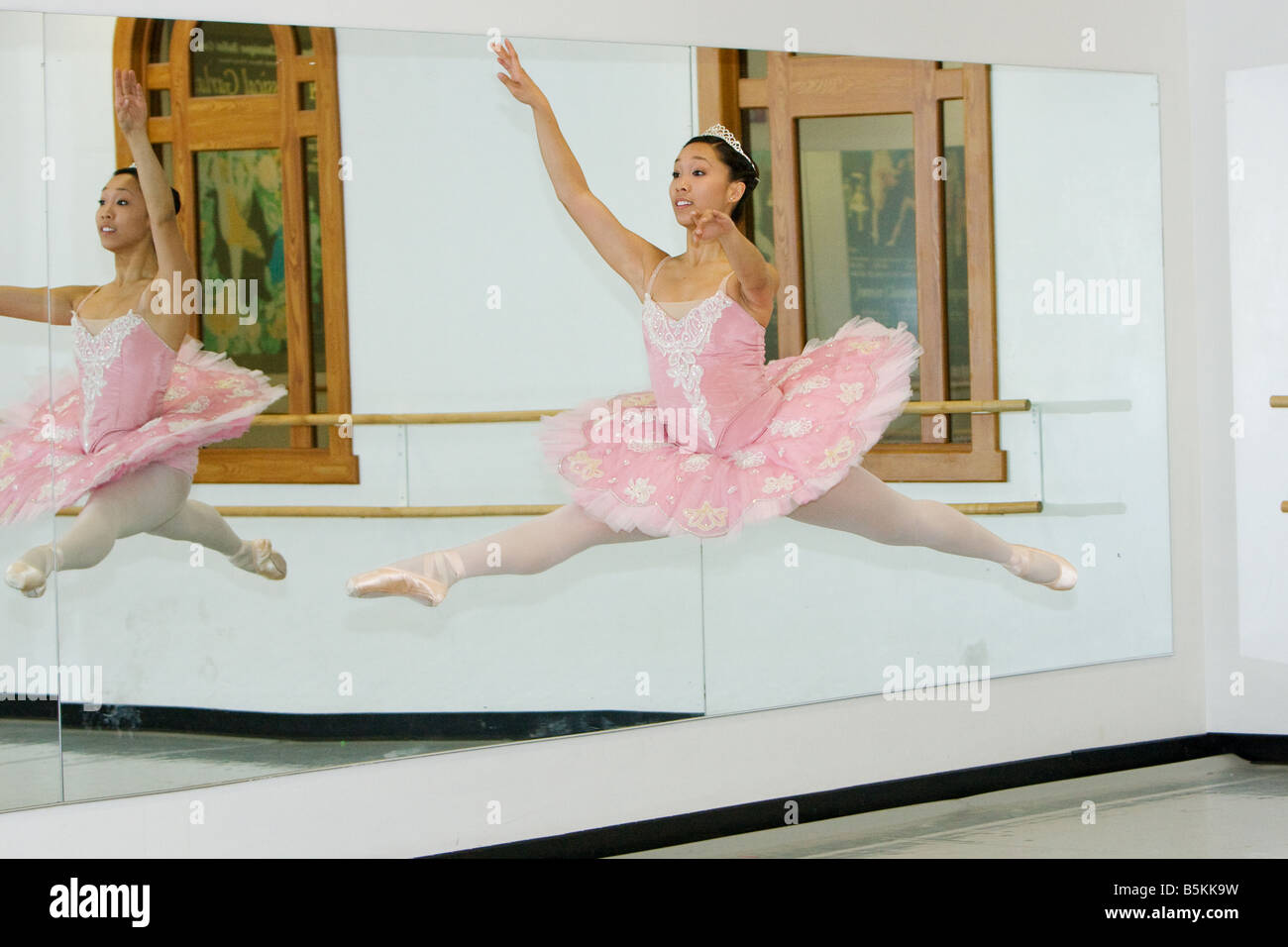 A ballerina in a pink tutu jumping through the air in front of a mirror. Stock Photo