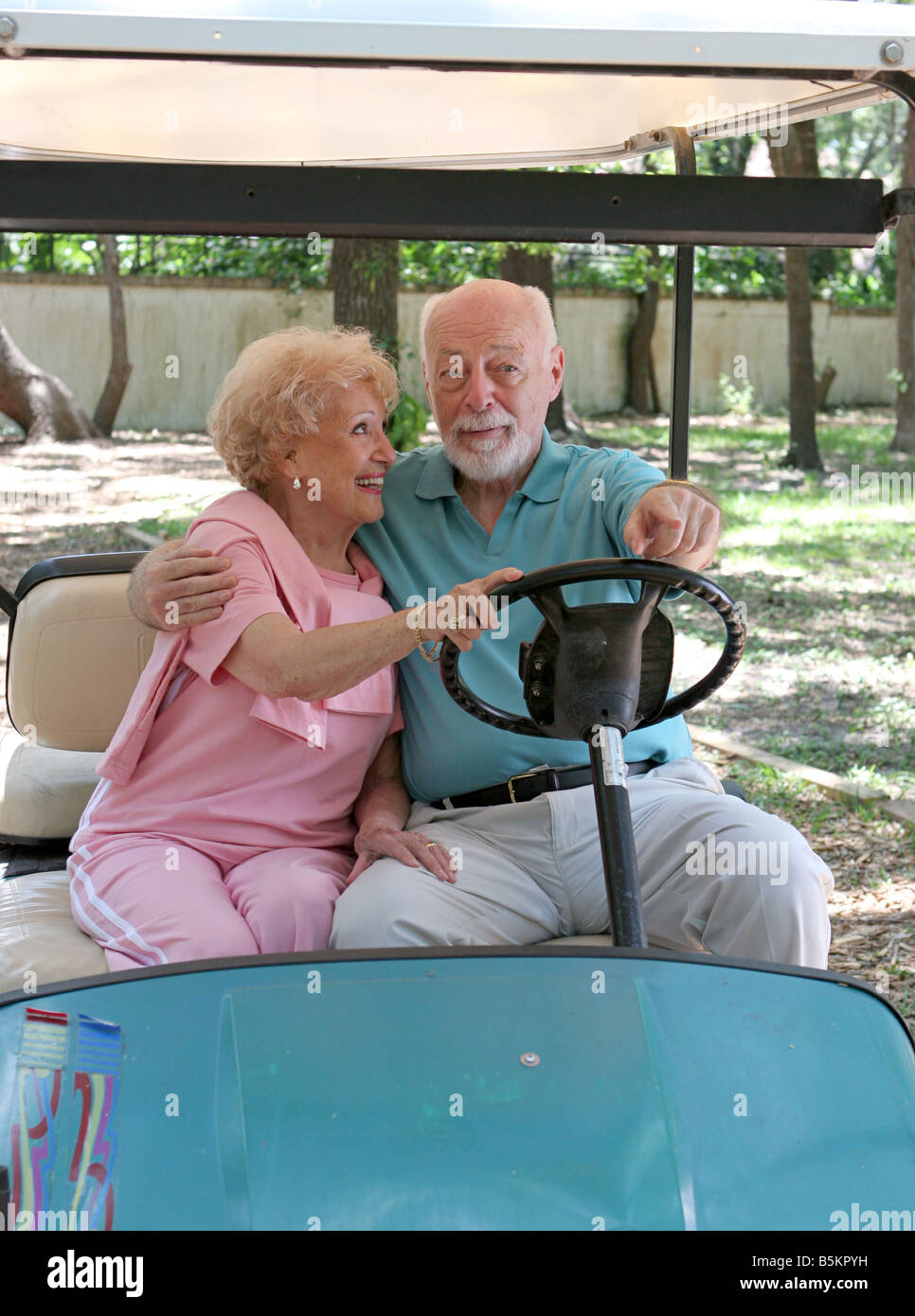 A senior couple riding in a golf card She is steering and he is pointing where to go Stock Photo