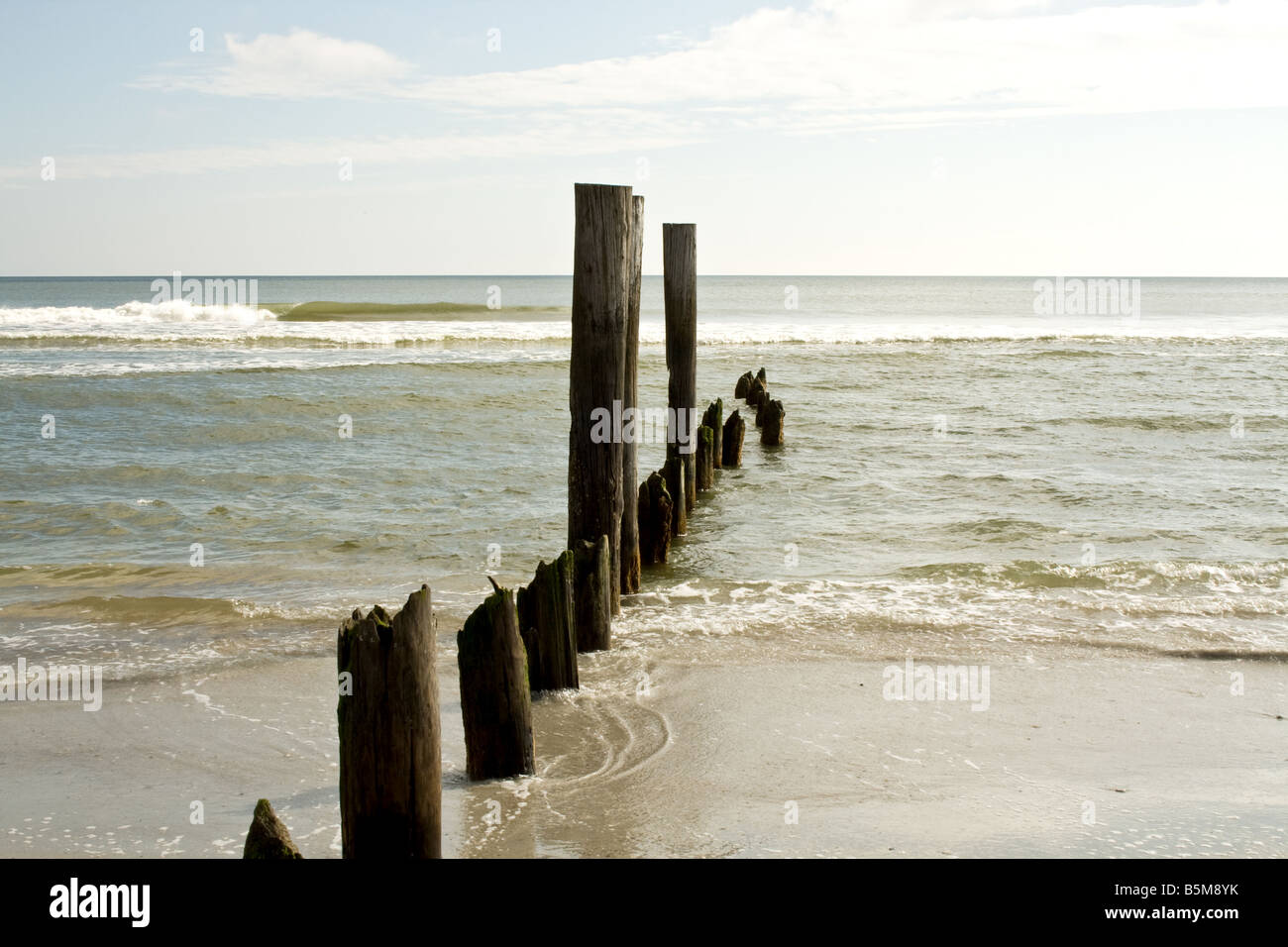 Old decaying wooden pilings leading into the ocean on a beach in Florida Stock Photo