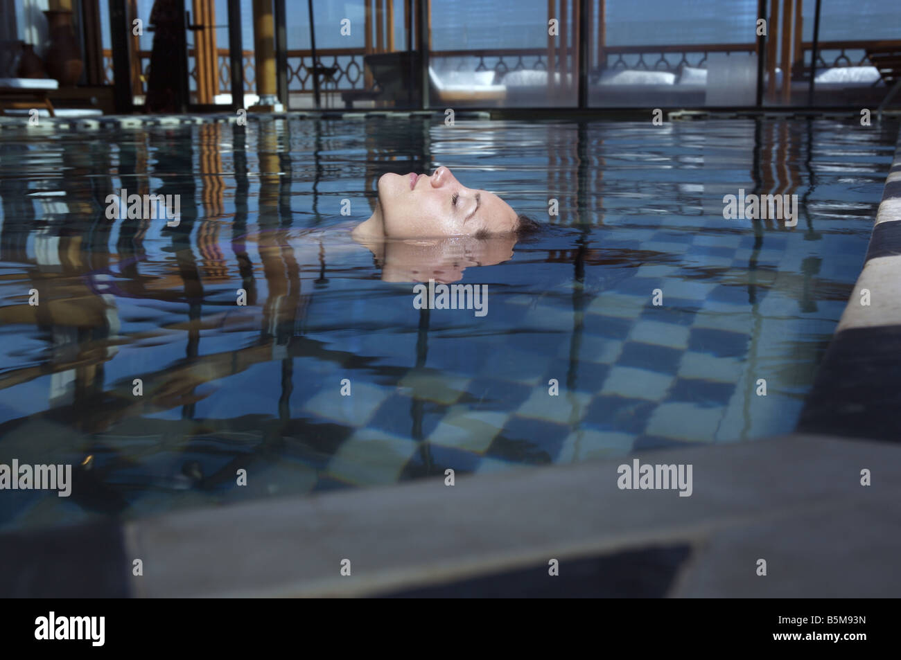 A woman floating in the pool with her face above water. Stock Photo
