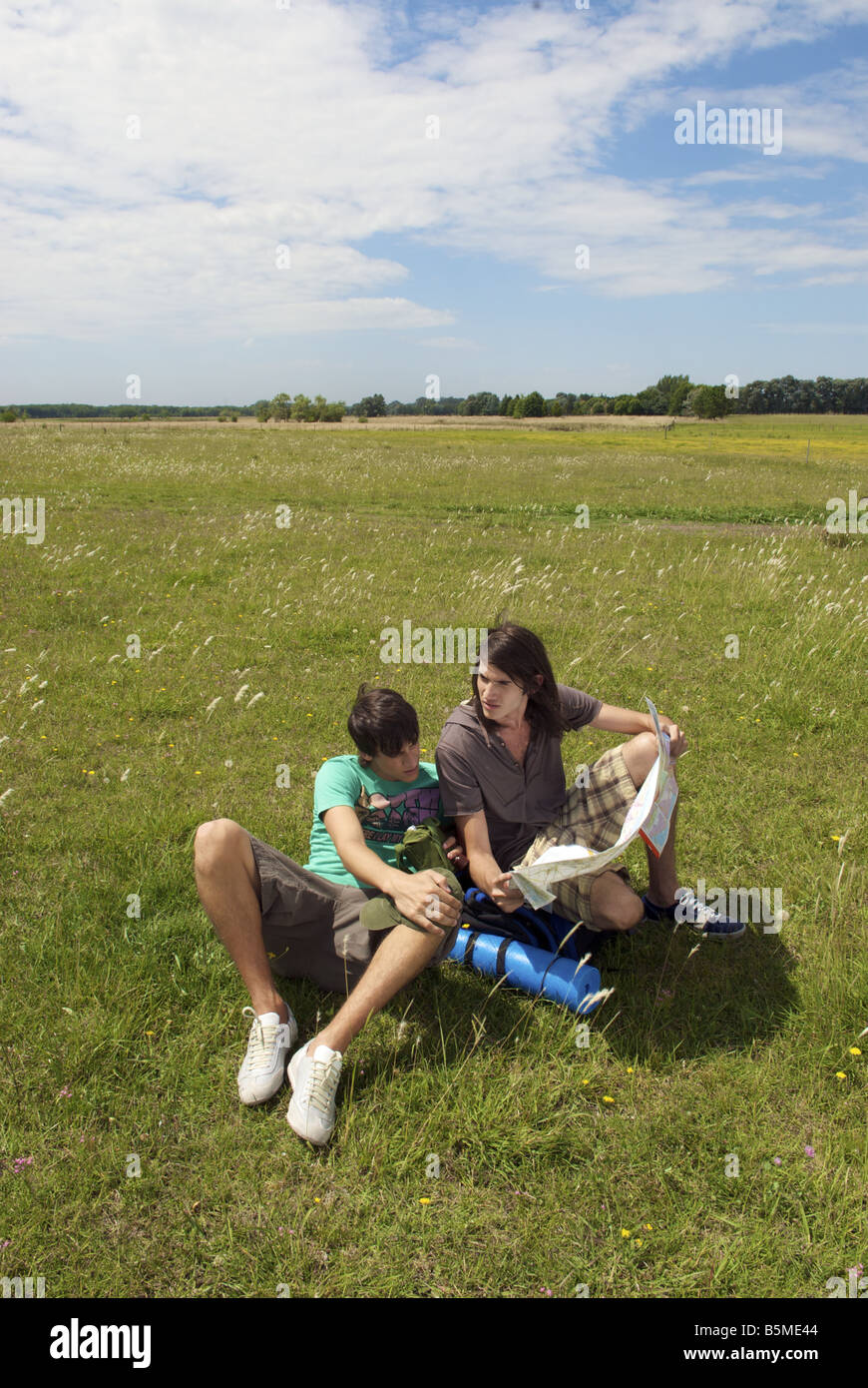 Two male backpackers sitting in a pasture and looking at a map Stock Photo