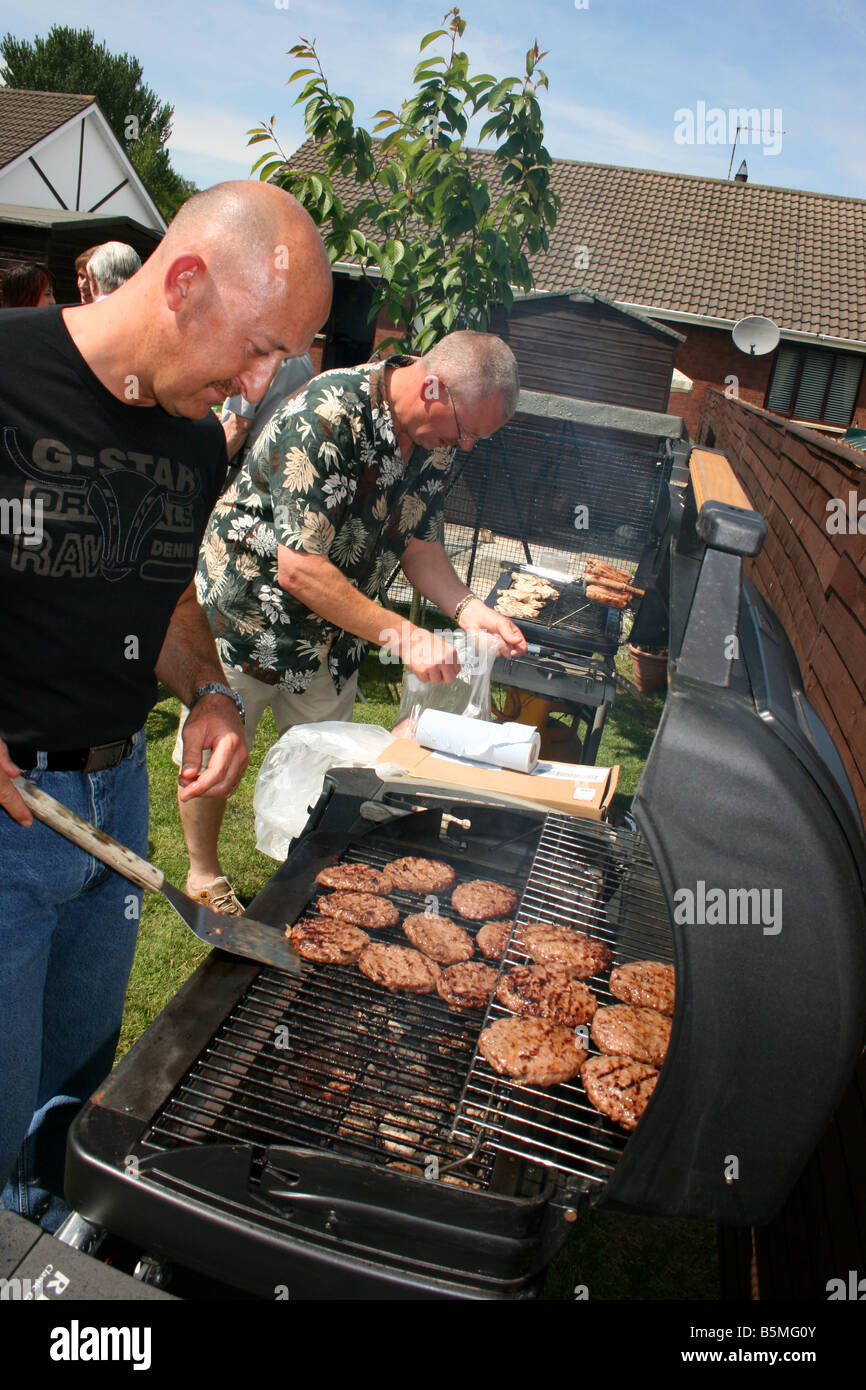 two men barbequing burgers at a summer garden party Stock Photo