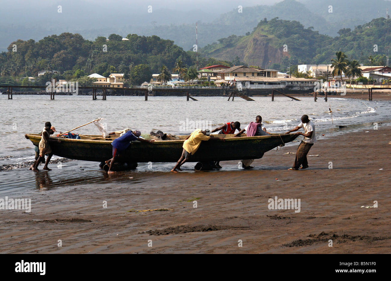 Fishermen dragging boat in at Limbé Cameroon West Africa Mount Cameroon in background Stock Photo