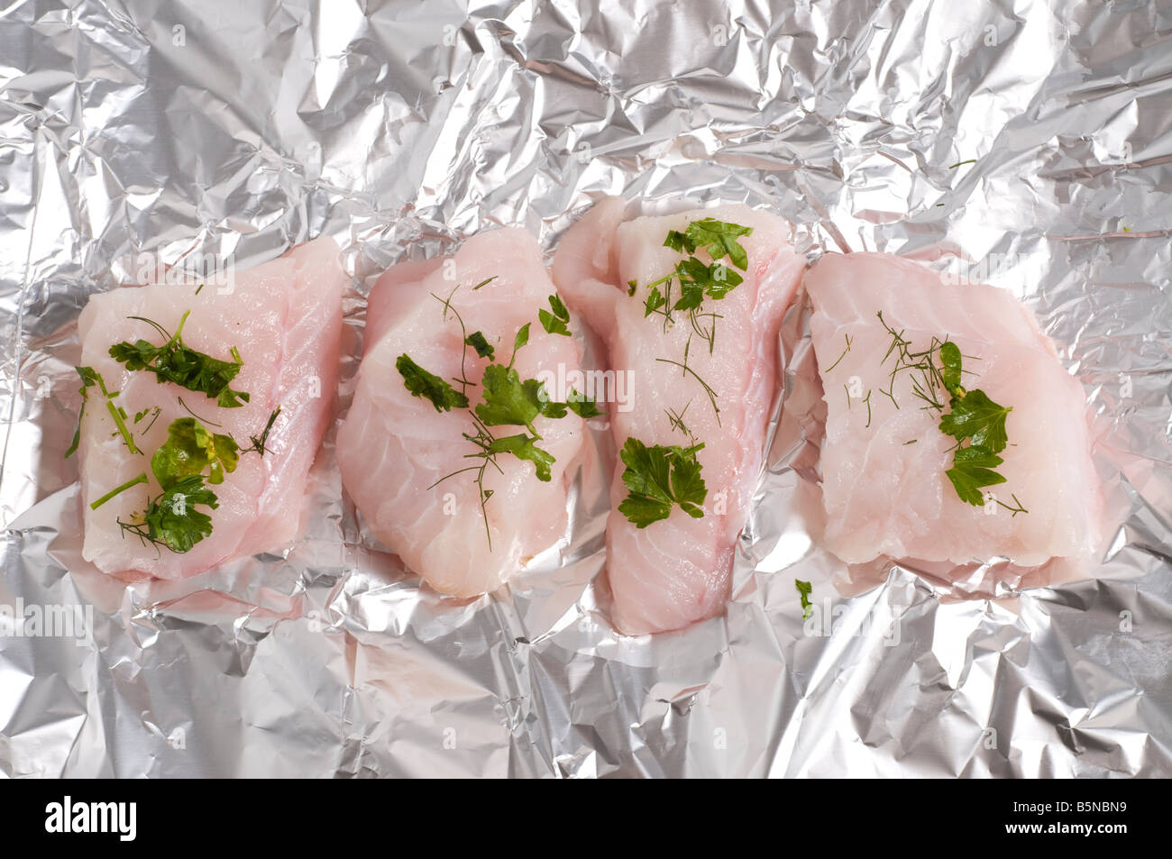 sliced monk fish and herbs laying on a sheet of tin foil Stock Photo