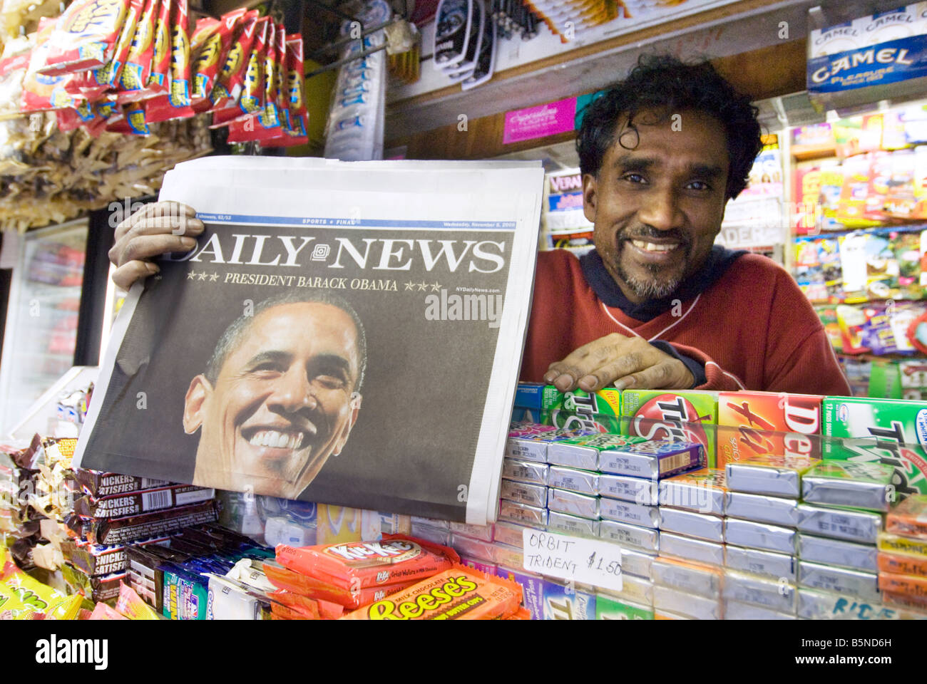 A newsstand owner in New York City holds up a newspaper announcing Barack Obama's historic presidential win in November 2008 Stock Photo