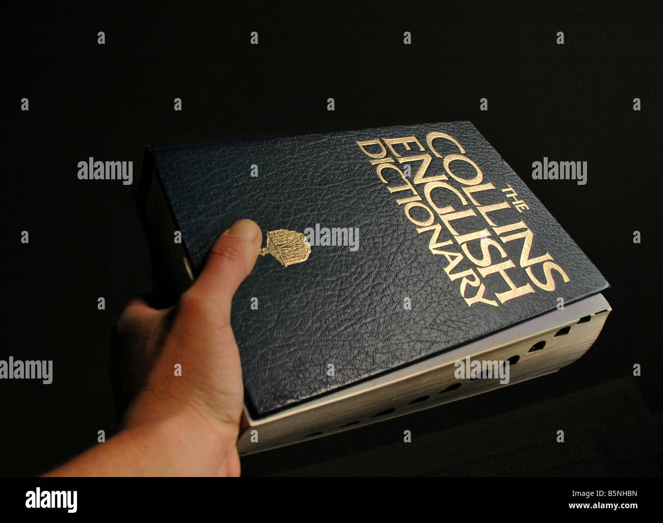An outstretched hand holding a dictionary against a black background