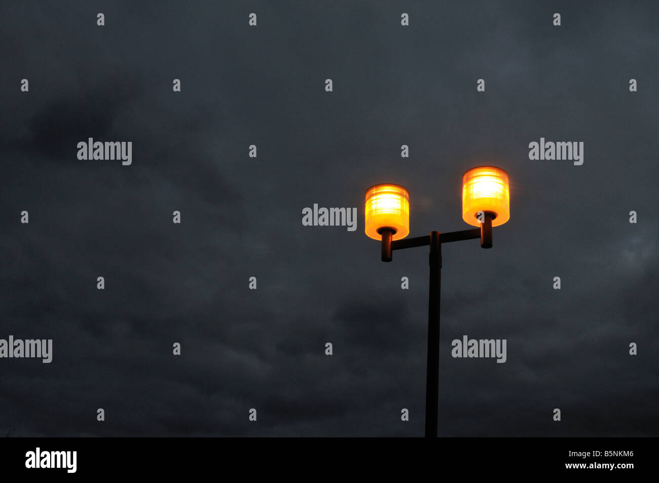 Dramatic eerie parking lot street lamps glowing at twilight against blue grey cloudy night sky Stock Photo