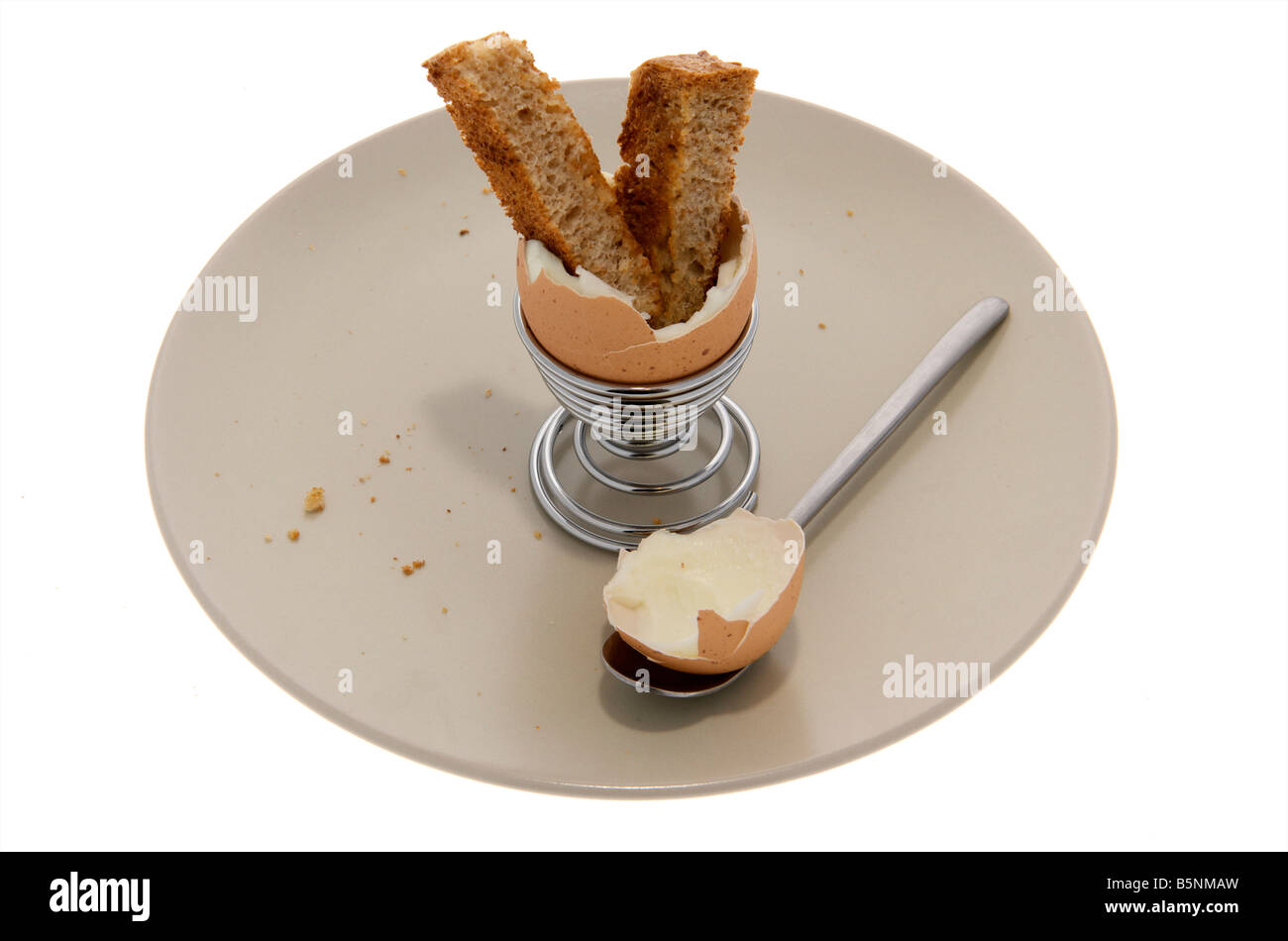 Empty Boiled egg sitting in egg cup on side plate with top cut off and a piece of toasted bread sticking out the top Stock Photo