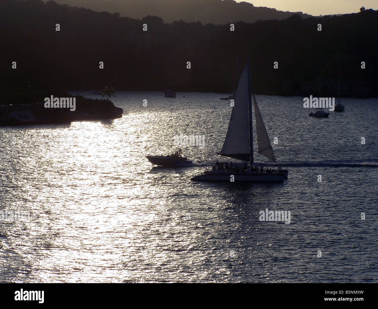 A sailboat and other types of watercraft silhouetted against the sunset