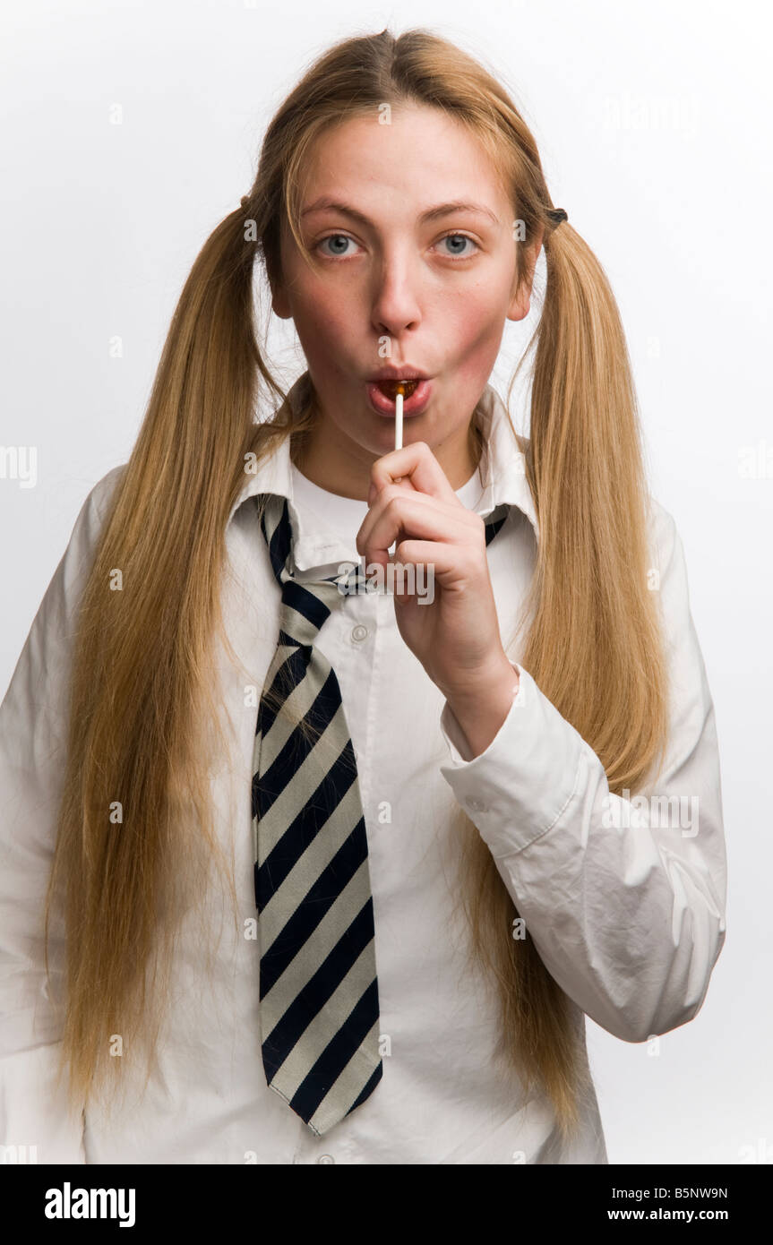 A Teenage schoolgirl wearing school uniform sucking a lollypop with her blonde hair in bunches UK Stock Photo