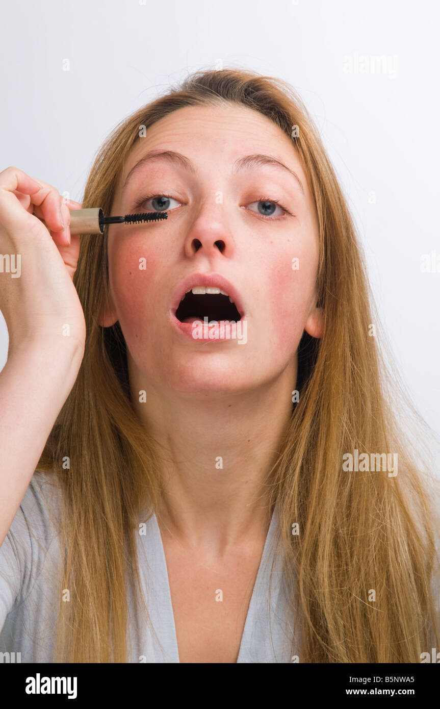 young blonde haired woman applying mascara to her eyelashes; putting on